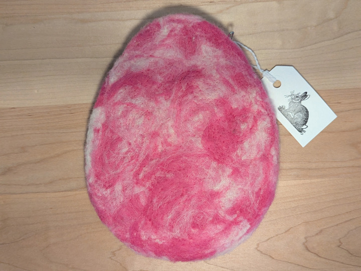 A felted egg-shaped trivet with a swirling pink and white design.