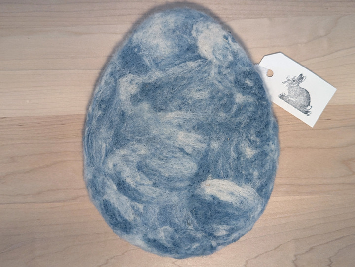 A felted egg-shaped trivet with a swirling blue and white design.