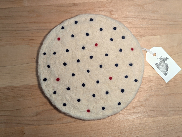 A felted circular white trivet with navy and red polka dots.