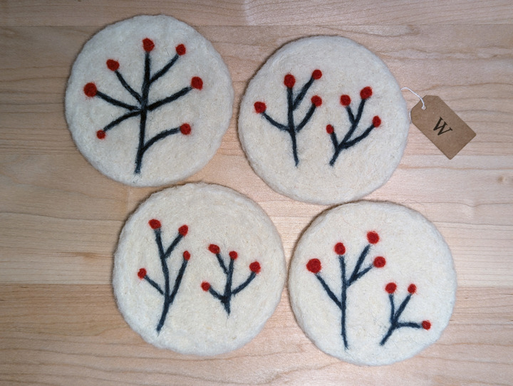 Felted circular white coasters with a stylized floral design in green and red.