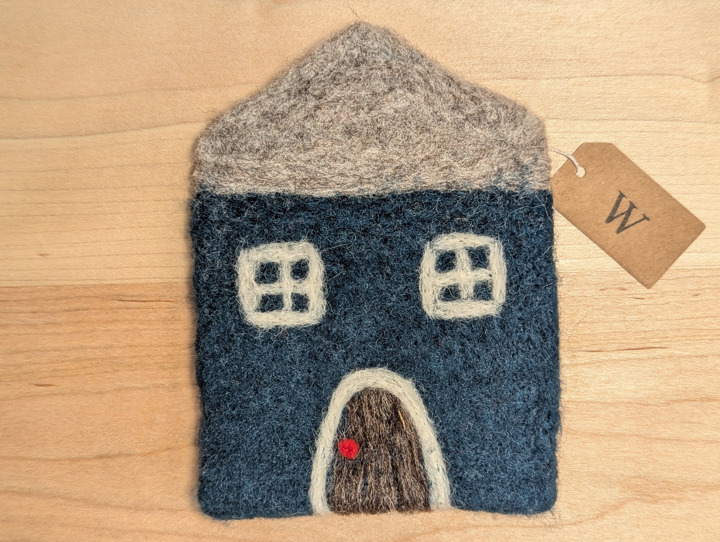 A felted coaster in the shape of a hunter green house with a heather grey roof and a brown door.