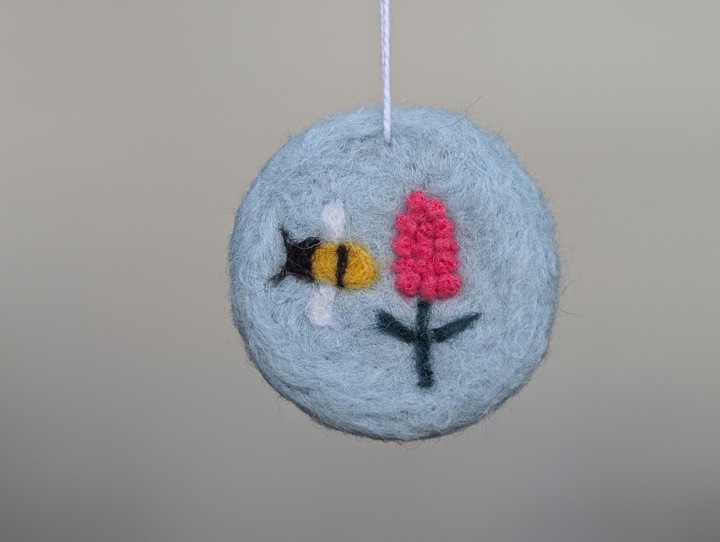 A round sky blue decoration with stylized flowers and a happy bee.