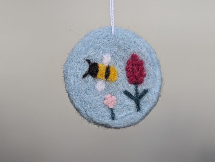 A round sky blue decoration with stylized flowers and a happy bee.