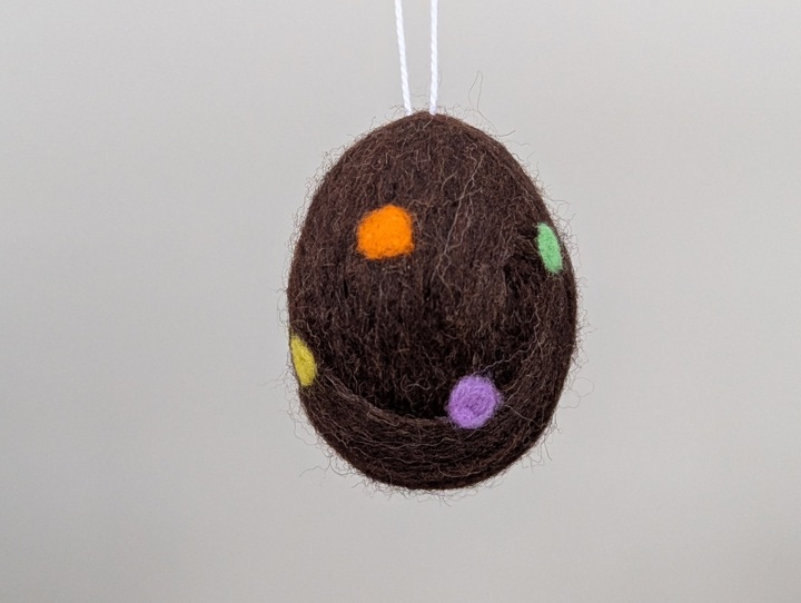 A felted chocolate brown egg with multicoloured polka dots.