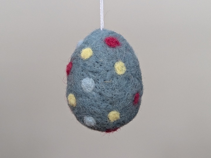 A felted blue egg with multicoloured polka dots.