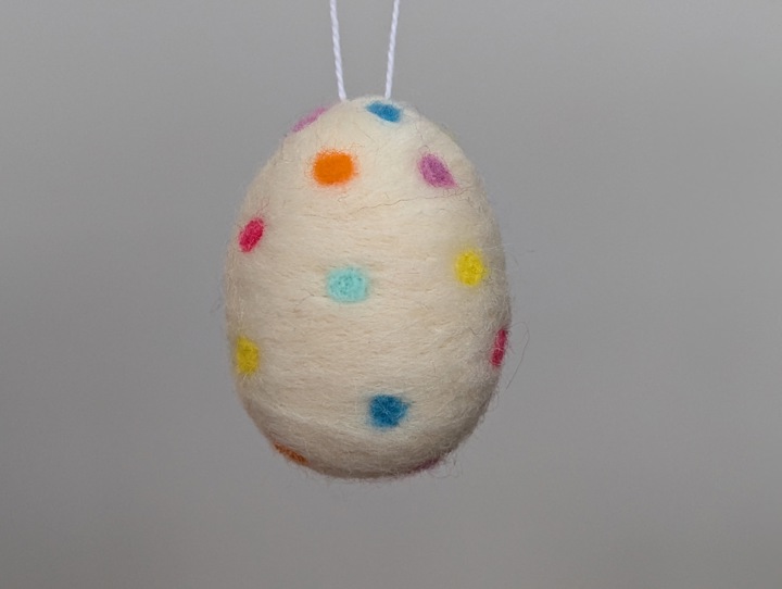 A felted white egg with multicoloured polka dots.