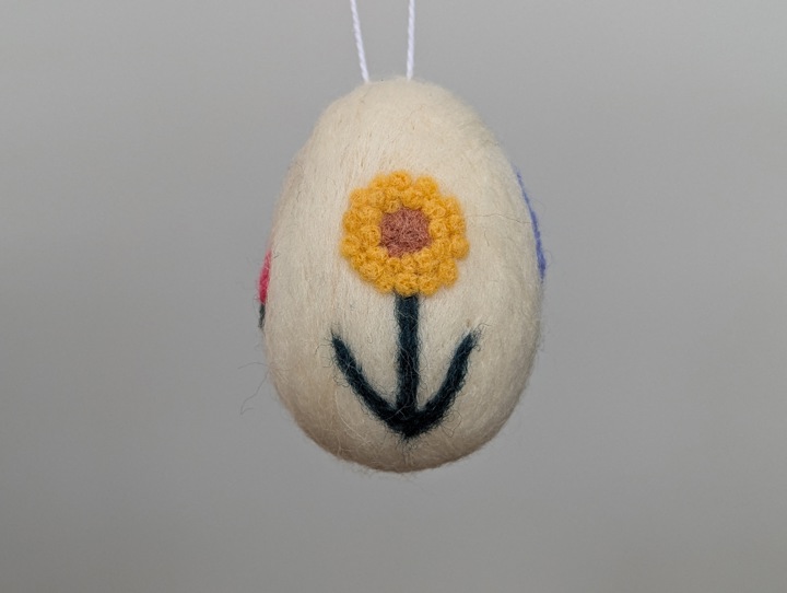 A felted white egg decorated with stylized flowers.