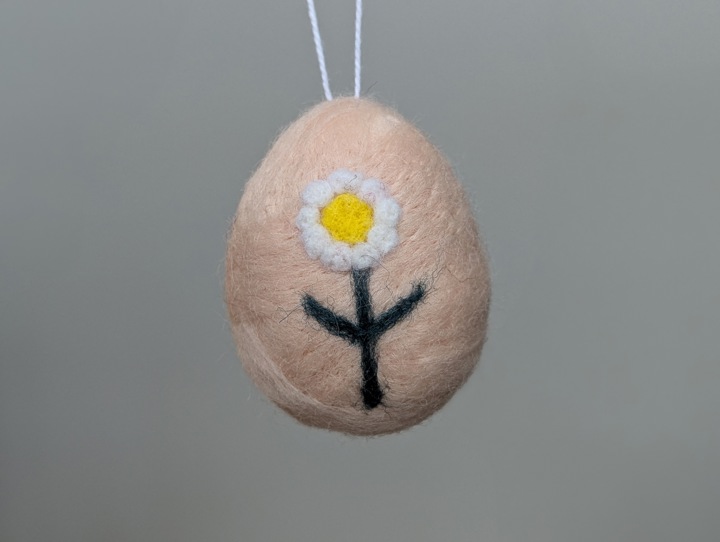 A felted pink egg decorated with stylized flowers.