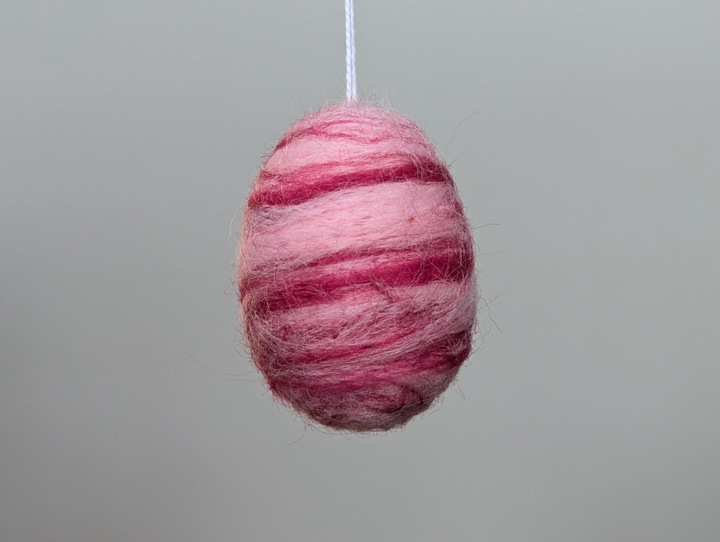 A felted egg decorated in a swirling burgundy and pink design.