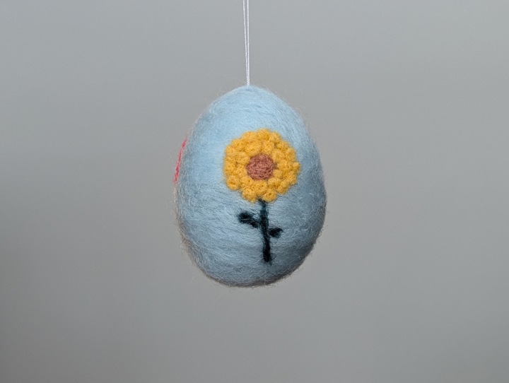 A small felted sky blue egg decorated with stylized flowers.