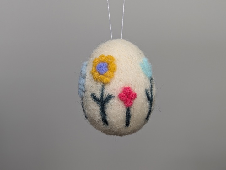 A small felted white egg decorated with stylized flowers.
