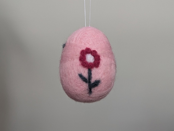 A small felted pink egg decorated with stylized flowers.