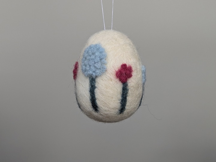 A small felted white egg decorated with stylized flowers.