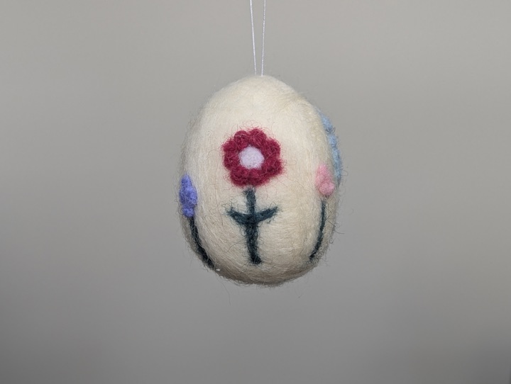 A small felted white egg decorated with stylized flowers.