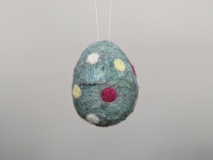 A small felted teal egg with multicoloured polka dots.