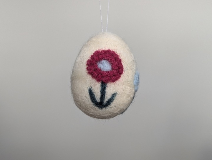 A small felted white egg decorated with stylized flowers.