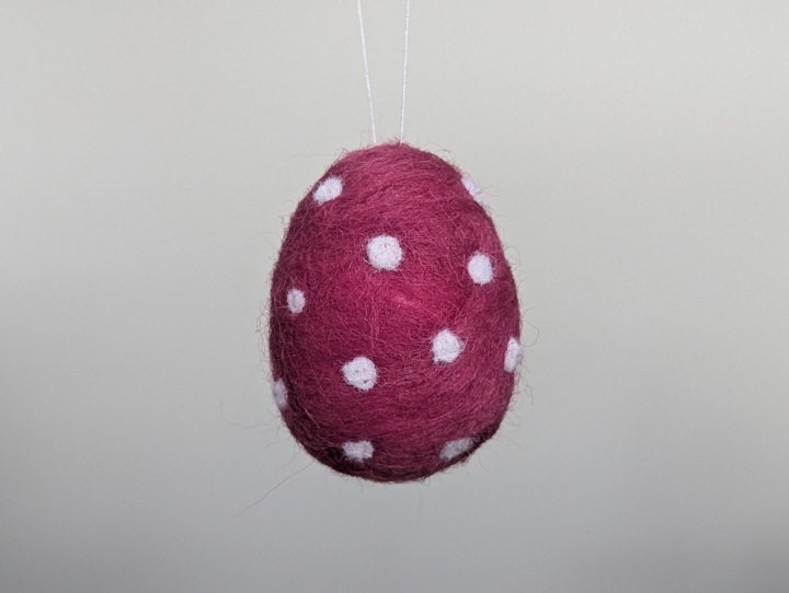 A small felted burgundy egg with white polka dots.
