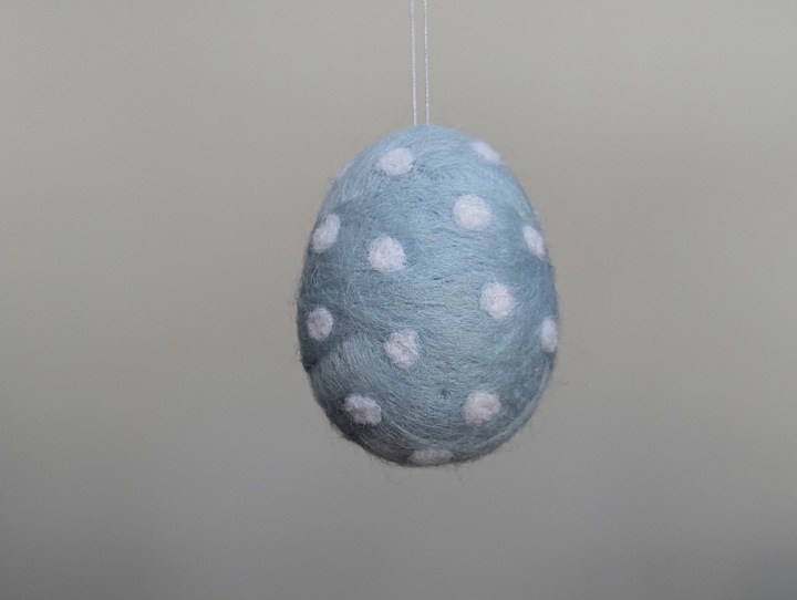 A small felted sky blue egg with white polka dots.