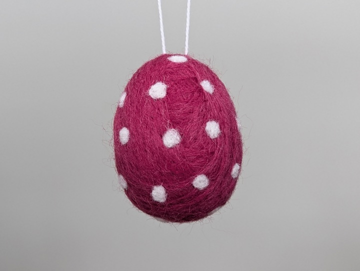 A felted burgundy egg with white polka dots.