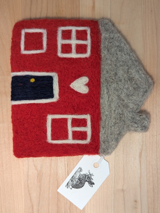A felted red house with a heather grey roof and a navy blue door with a heart motif above it.