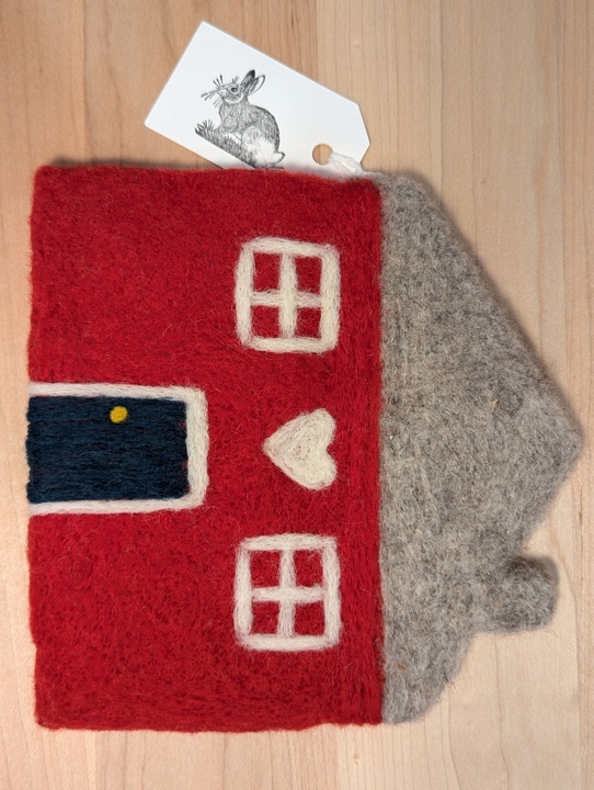 A felted red house with a heather grey roof and a hunter green door with a heart motif above it.