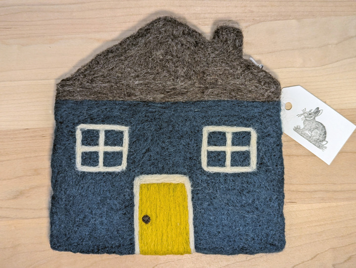 A felted hunter green house with a heather grey roof and a yellow door.