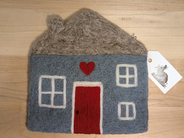 A felted sky blue house with a heather grey roof and a red door with a heart motif above it.