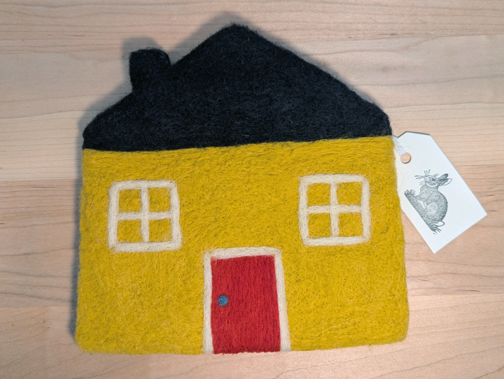 A felted yellow house with a black roof and a red door.