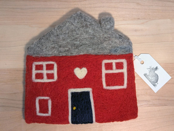 A felted red house with a heather grey roof and a navy door with a heart motif above it.