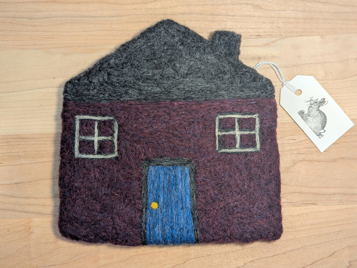 A felted plum house with a black roof and blue door.