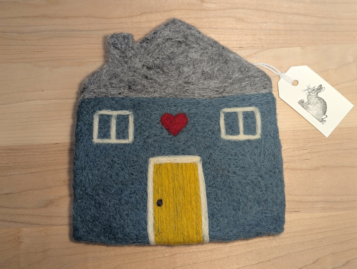 A felted blue house with a heather grey roof and a mustard door with a heart motif above it.