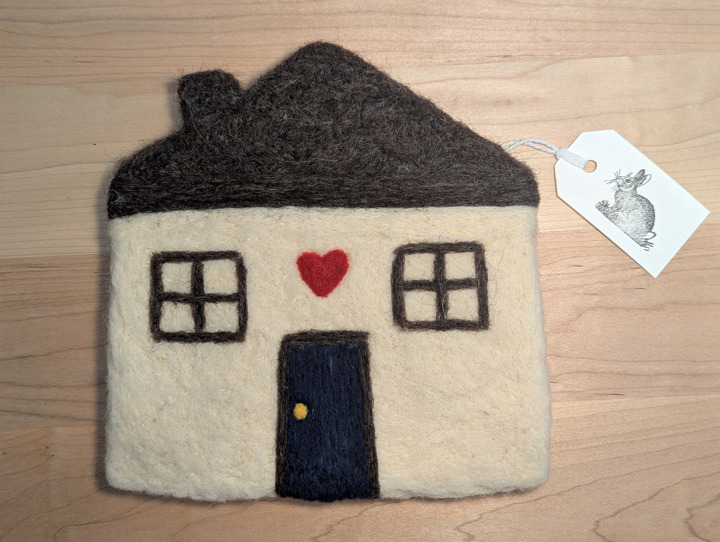 A felted white house with a brown roof and a navy blue door with a heart motif above it.
