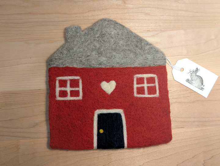 A felted red house with a heather grey roof and a navy door with a heart motif above it.