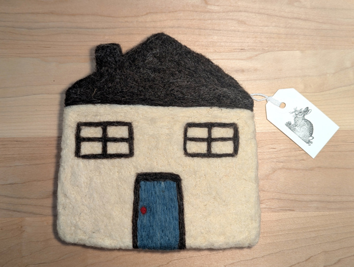A felted white green house with a brown roof and blue door.