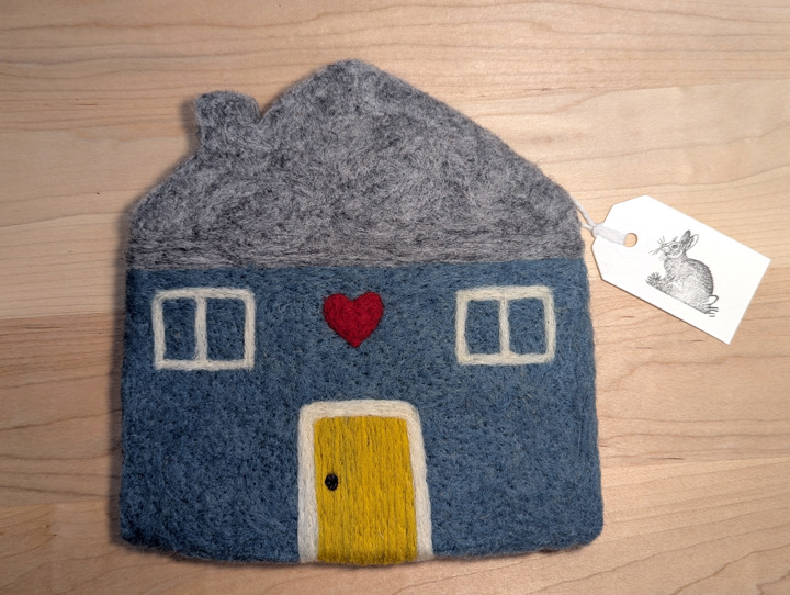 A felted country blue house with a heather grey roof and a yellow door with a heart motif above it.