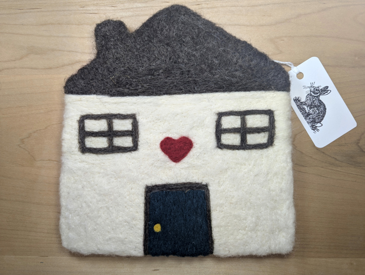 A felted white house with a brown roof and a navy blue door with a heart motif above it.