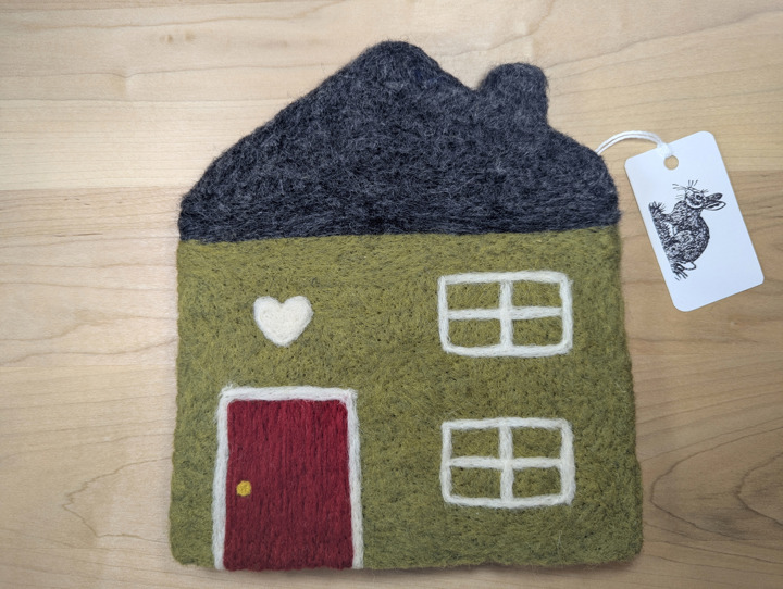 A felted olive green house with a dark grey roof and red door with a white heart motif above it.