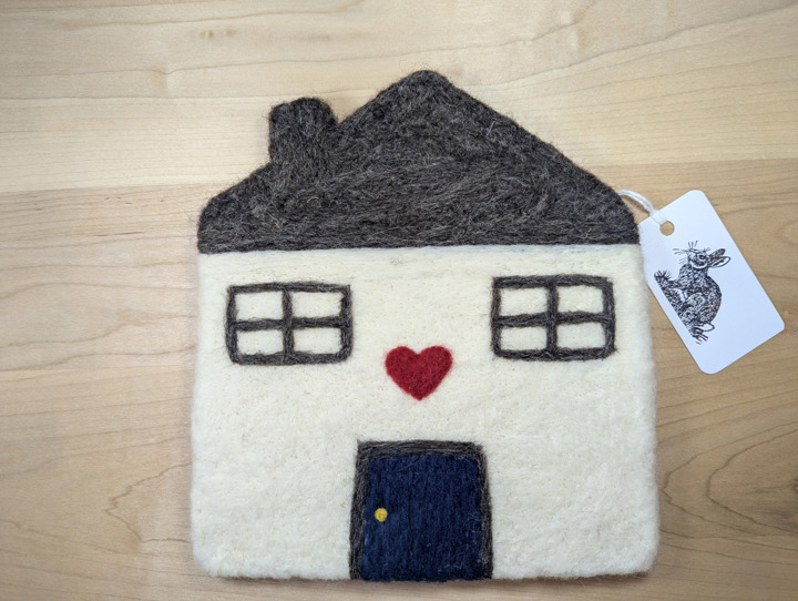 A felted white house with a brown roof and a navy blue door with a heart motif above it.