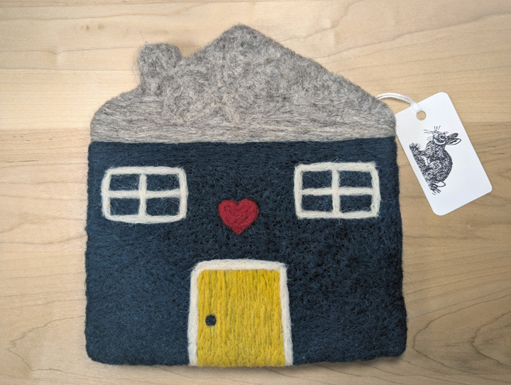 A felted hunter green house with a light grey roof and a yellow door with a heart motif above it.