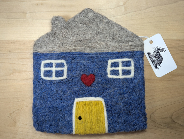 A felted heather blue house with a grey roof and a yellow door with a heart motif above it.
