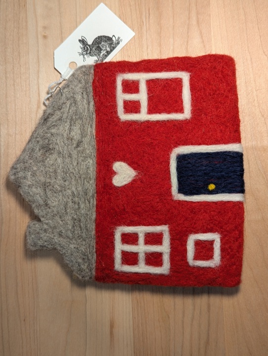 A felted red house with a heather grey roof and a black door with a heart motif above it.