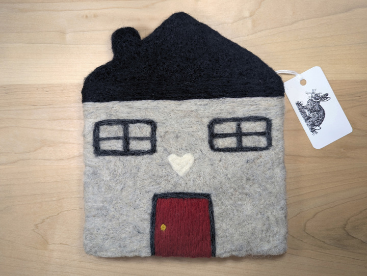 A felted light grey house with a black roof and a red door with a white heart motif above it.