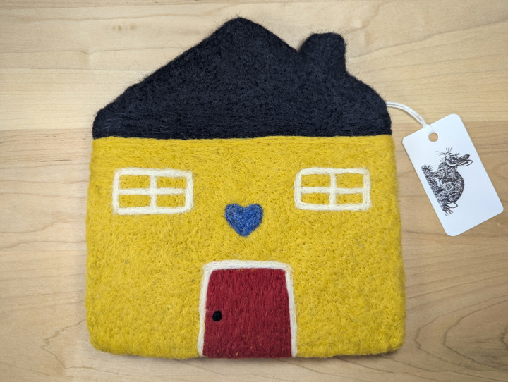 A felted yellow house with a black roof and a red door with a blue heart motif above it.