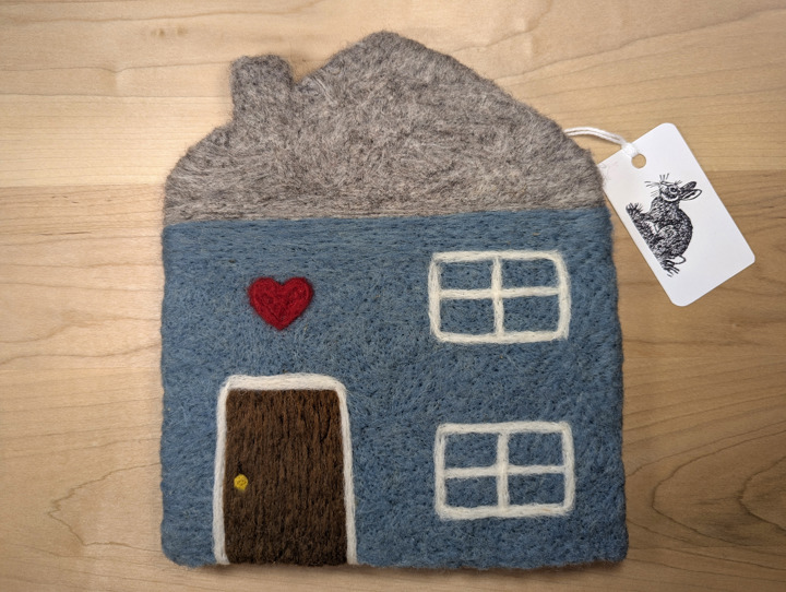 A felted country blue house with a grey roof and a brown door with a heart motif above it.