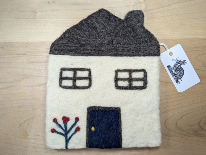 A felted white house with a brown roof, a navy blue door and red flowers growing at the front.
