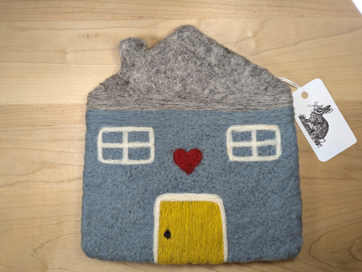 A felted country blue house with a grey roof and a yellow door with a heart motif above it.