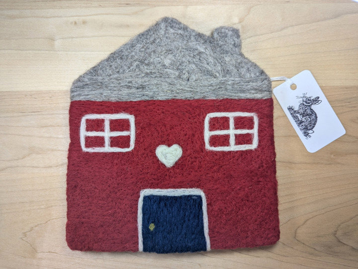 A felted red house with a light grey roof and a navy blue door with a white heart motif above it.