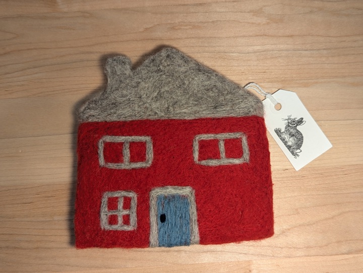 A felted red house with a heather grey roof and a blue door.