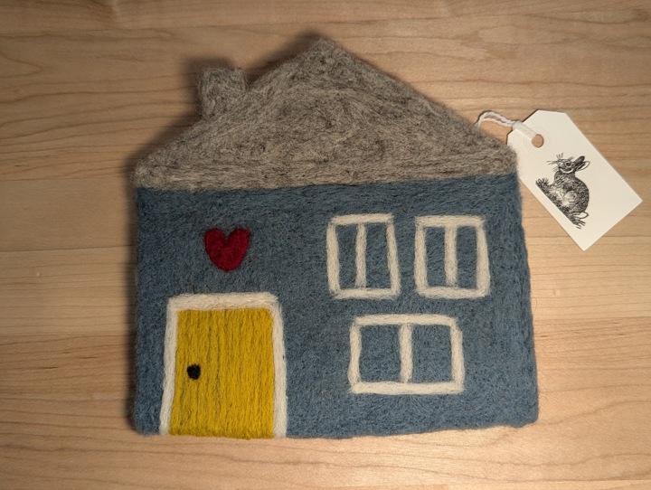 A felted blue house with a heather grey roof and a mustard door with a heart motif above it.
