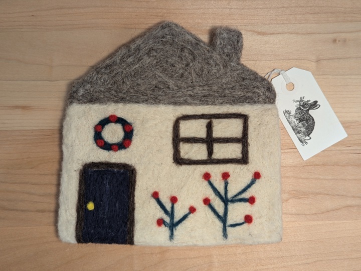 A felted white house with a heather grey roof, a black door, flowers and a wreath.
